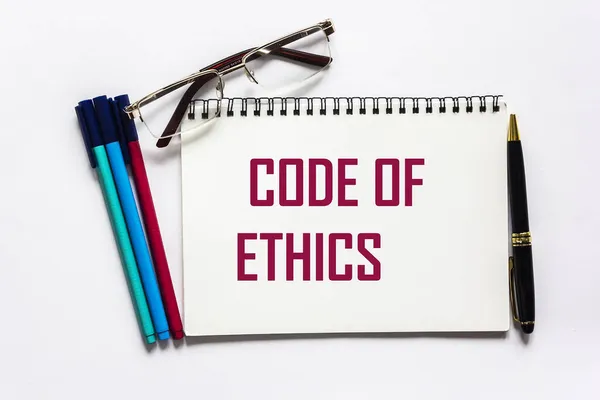 Code of ethics word written on a notebook and a white background, near felt-tip pens, a pen and glasses.