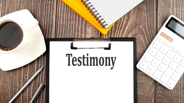 Kahve, hesap makinesi ve defterle kağıda yazılmış TESTIMONY metni. İş dünyası