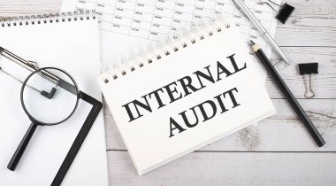 Masaüstünde kalem, ofis araçları ve grafiklerle birlikte INTERNAL AUDIT metni bulunan not defteri.