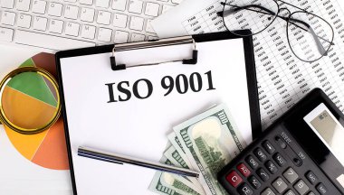 ISO 9001 'i ofis masasına beyaz arkaplanda klavye, dolar, hesap makinesi, malzeme ve analiz çizelgesiyle birlikte gönder..