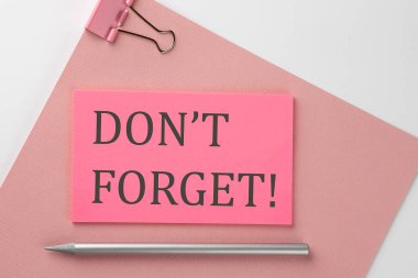 Pembe kağıt üzerine pembe etiket, beyaz arka planda kalem ve metin. Unutma.