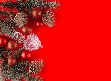 Noel kırmızı süslemeleri, köknar ağacı dalları ve kırmızı arka planda toplar. Boşluğu kopyala