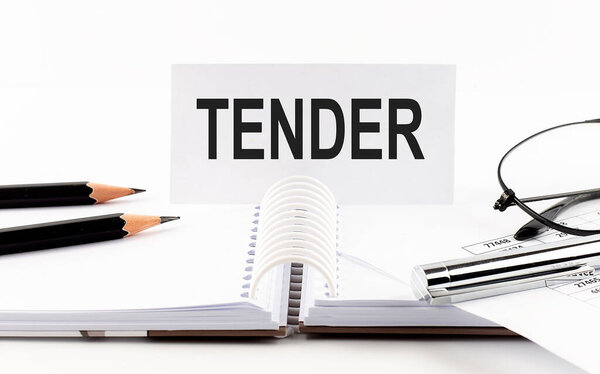 TENDER on paper card, pen, pencils, glasses, financial documentation on table - business
