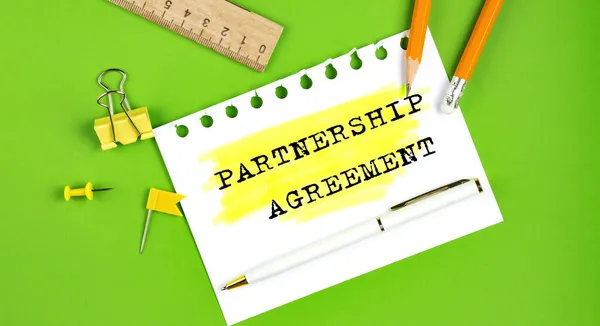 オフィスツールと緑の背景に表示されるテキストパートナーシップ契約のサイン — ストック写真