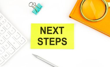 Beyaz arkaplanda, hesap makinesi ve defterin yanında NEXT STEPS metni olan etiket