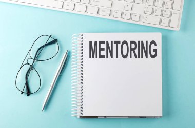 Klavye, not defteri, mavi zemin üzerinde kalem ve gözlükler.