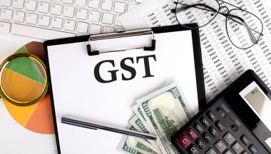 Beyaz arkaplanda klavye, dolar, hesap makinesi, malzeme ve analiz çizelgesi olan ofis masasında GST metni.
