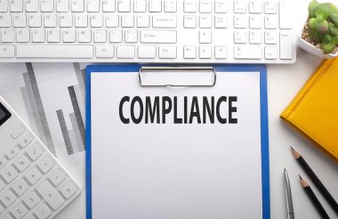 Klavye, grafik, hesap makinesi ve defter ile kağıda yazılmış COMPLIANCE
