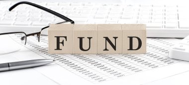 Klavye, hesap makinesi, çizelge, gözlük ile ahşap küpte FUND yazıyor.