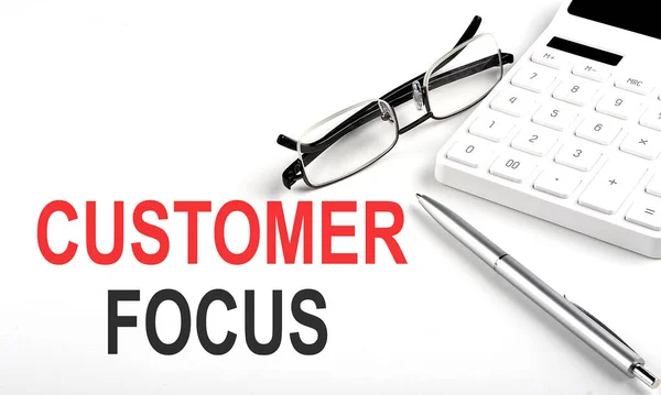 CUSTOMER FOCUS Concept. Calculator,pen and glasses on the white background