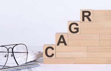 Klavye ve gözlüklü beyaz masada CAGR harfli tahta küpler.