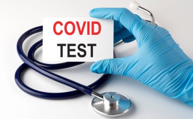 Üzerinde COVID test malzemeleri, haplar ve steteskop olan bir kart. Tıbbi metin