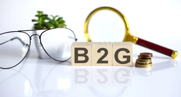 B2G Concept Wooden Cubes Flower Glasses Coins Magnifier White Background — Stockfoto