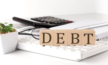 DEBT written on wooden cube on the keyboard with office tools