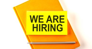 Text WE ARE HIRING on sticker on the yellow notebook