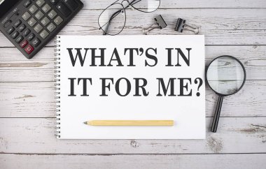 Blank notebook with text WHAT'S IN IT FOR ME on the white background with calculator and office tools.
