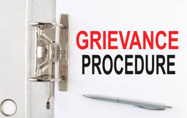 Kağıt klasörün üzerinde kalemle GRIEVANCE PROCEDURE metni. İş dünyası