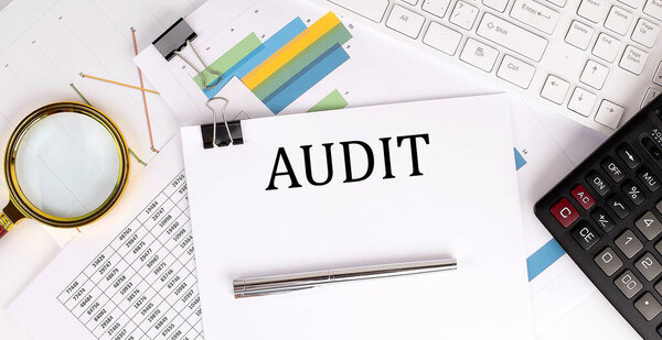 AUDIT text on the white paper on light background with charts paper ,keyboard and calculator
