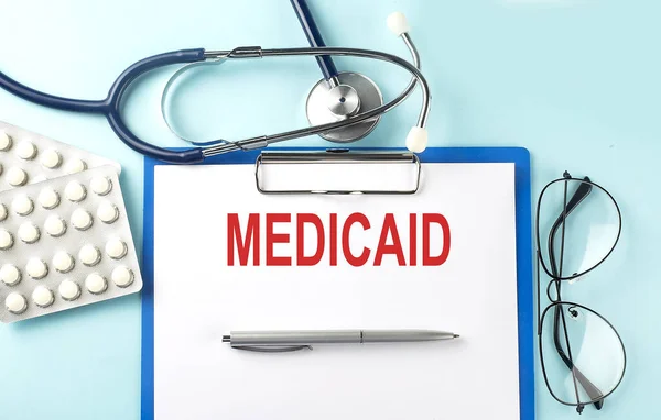 Mavi zemin üzerinde steteskop ve haplarla metin MEDICAID 'i olan kağıt