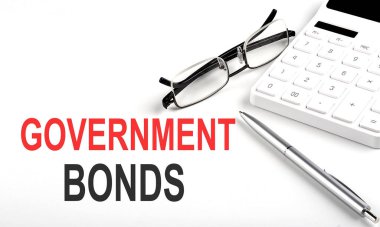 HÜKÜMET BONDS kavramı. Beyaz arkaplanda hesap makinesi, kalem ve gözlük