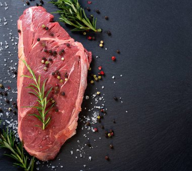Biberiyeli çiğ biftek ve siyah arka planda baharatlar..