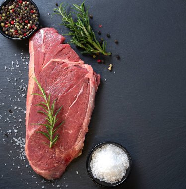 Biberiyeli çiğ biftek ve siyah arka planda baharatlar. Boşluğu kopyala