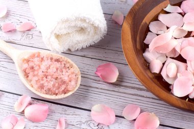 Ahşap arka planda pembe tuz ve beyaz havluyla ahşap bir kasede gül yaprakları