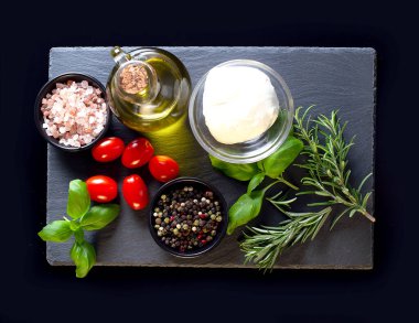 Mutfak arka planında siyah arka planda mutfak tahtası, otlar ve çeşitli baharatlar var.