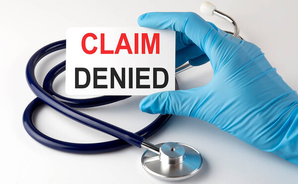 Card text CLAIM DENIED supplies, pills and stethoscope. Medical concept.
