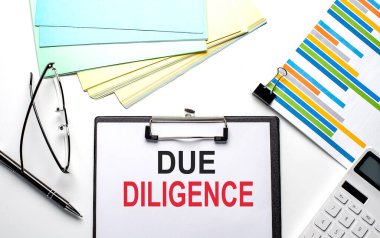 Dosya, renk kağıdı ve hesap makinesiyle kağıt üzerinde DUE DILIGENCE metni