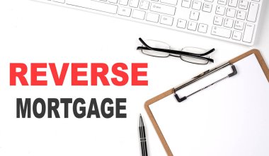 Klavye, kağıt sayfa ve kalem ile beyaz arkaplanda yazılan REVERSE MortGage metni