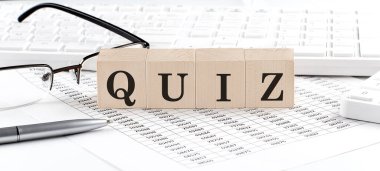Klavye, hesap makinesi, çizelge, gözlük ile ahşap küp üzerine yazılan QUIZ. İş