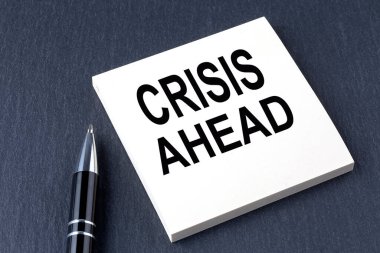 CRISIS AHEAD etiketli metin ve siyah arkaplan üzerinde kalem