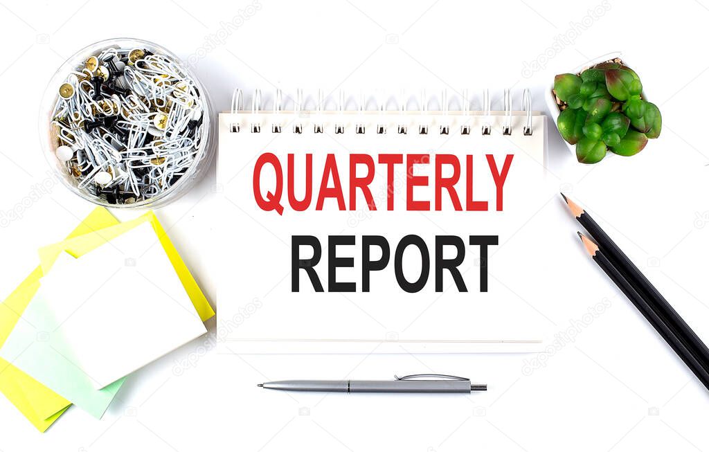 QUARTERLY REPORT text on the notebook with office supplies on white background