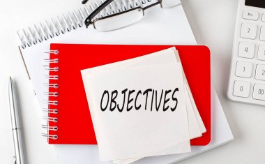 Not defterindeki etiket üzerinde kalem ve hesap makinesiyle OBJECTIVES sözcüğü