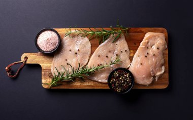 Biber, tuz ve ahşap bir tahtada biberiyeli çiğ tavuk göğsü fileto, siyah arkaplan.