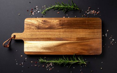 Siyah arka planda biber, tuz ve taze biberiye ile ahşap kesme tahtası, kopyalama alanı