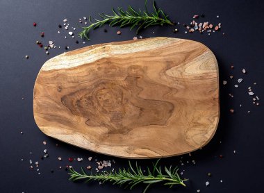 Siyah arka planda biber, tuz ve taze biberiye ile ahşap kesme tahtası, kopyalama alanı