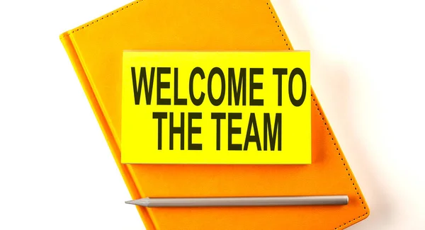 Text WELCOME TO THE TEAM on sticker on the yellow notebook