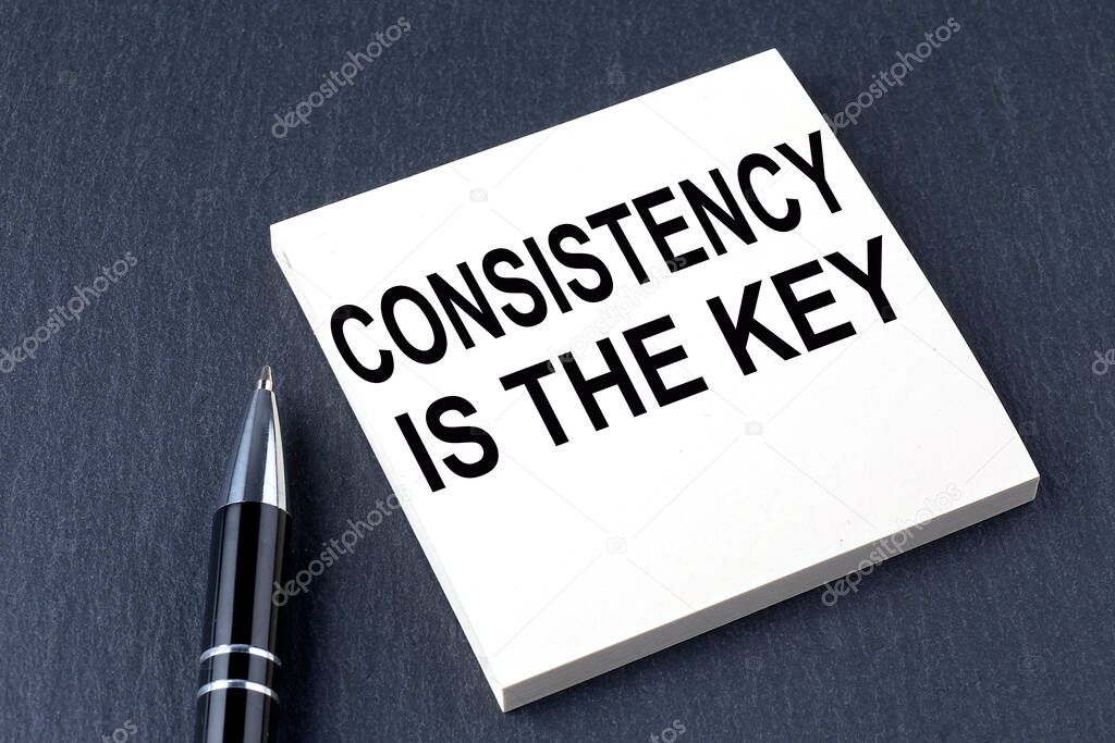 CONSISTENCY IS THE KEY text on the sticker with pen on black background