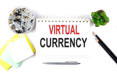 Not defterine beyaz arka planda ofis malzemeleriyle birlikte VIRTUAL CURRENCY metni