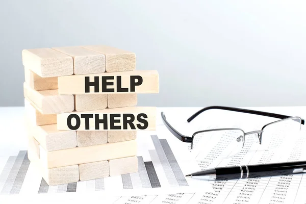 HELP OTHERS is written on a wooden blocks on a chart background