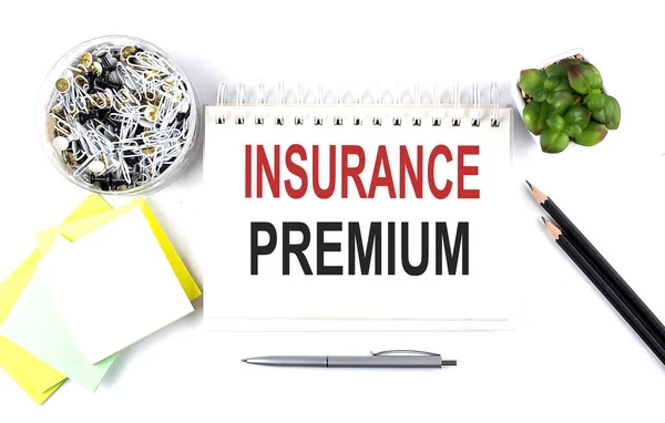 INSURANCE PREMIUM text on notebook with office supplies on a white background