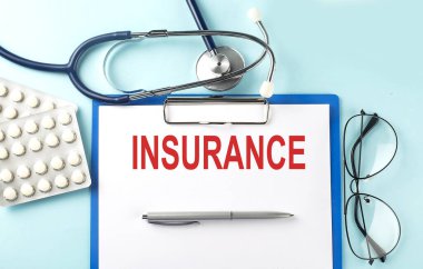 Mavi zemin üzerinde steteskop ve haplarla INSURANCE metni olan kağıt