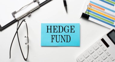 Beyaz zemin üzerinde HEDGE FUND metni bulunan çizelge, hesap makinesi ve kağıda sahip çıkartmalar