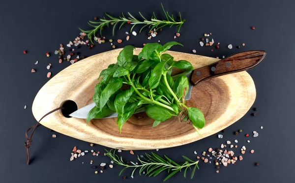 bunch of fresh organic basil on a knife on cutting board with spices on black background