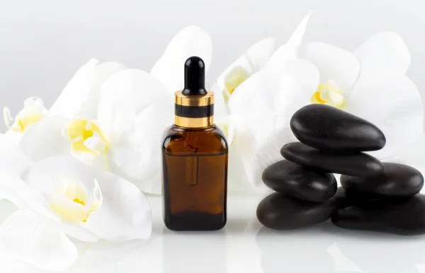 A brown bottle of cosmetic oil stands on black stone with beautiful orchids . Spa concept