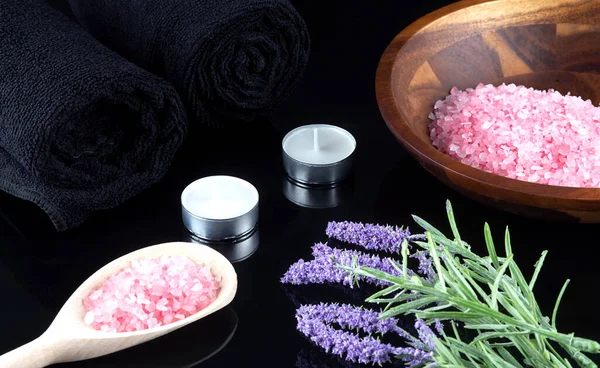 Black spa setting with black towels, white orchids and pink sea salt on a black background. Spa concept