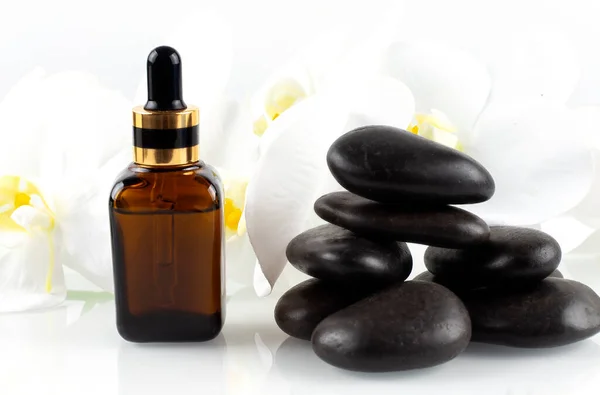 A brown bottle of cosmetic oil stands on black stone with beautiful orchids . Spa concept