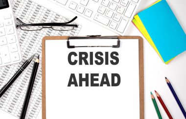Beyaz arkaplan üzerinde CRISIS AHEAD metin panosu ve klavye ve grafik.